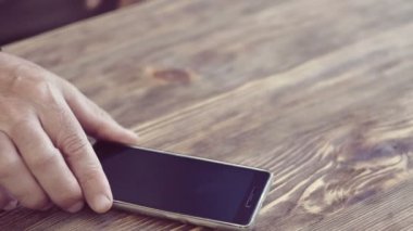 Adam el cep telefonu ve seyretmek ahşap masanın üstüne koyar. yeşil ekran