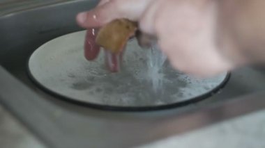 adam lavaboya bir sünger ve deterjan ile çatal yıkar