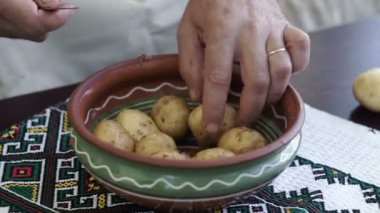 Ev mutfak patates soyarken oldu. A adam elinde bir bıçak ve patates soyma ve bir kase içinde temiz. Evde yemek pişirme.