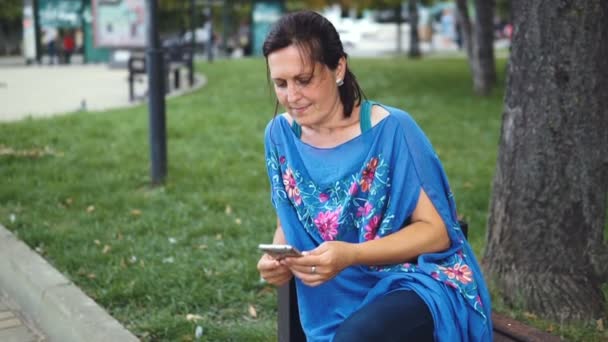 在户外智能手机的惊人的女人的肖像 漂亮的黑发使用她的手机与触摸屏站在公园 — 图库视频影像
