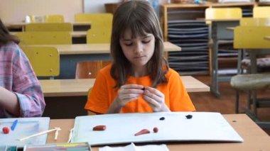 Masada oturan iki küçük kız renkli modelleme hamuru odasında yapılmış farklı rakamları sculpts.