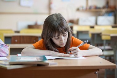 Little girl writing something in copybook and sitting at table clipart