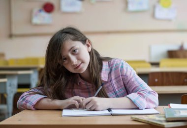 Küçük kız deftere bir şeyler yazıyor ve masada oturuyor.
