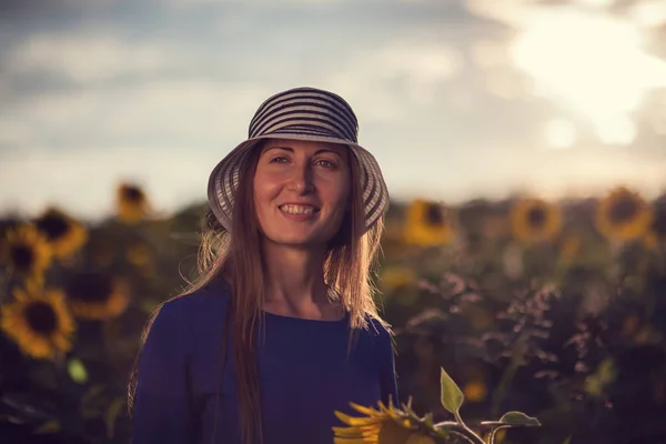 Dívka v modrých šatech listy s kloboukem v poli slunečnic — Stock fotografie