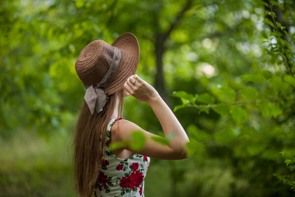 Портрет красивой элегантной женщины в светло-белом платье и шляпе, стоящей в летнем парке
.