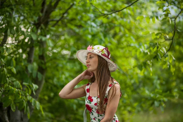 光の白いドレスと帽子の夏の公園に立っている美しいエレガントな女性の肖像画 — ストック写真