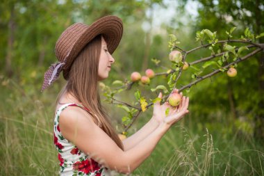 güzel kız elma Bahçe arka plan üzerinde duruyor. Kız bir yazlık elbise giymiş.