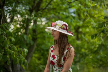 Işık beyaz elbise ve şapka yaz parkta duran güzel zarif bir kadın portresi.