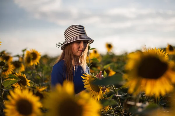 女孩在蓝色礼服叶子与帽子在向日葵领域在日落 — 图库照片