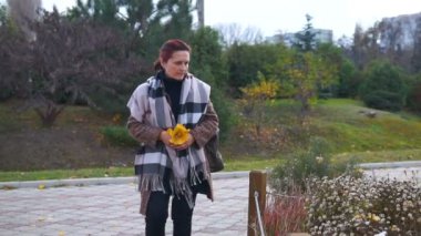 Kadın parkta sarı kaplı ağaçlar arasında yürüyor..