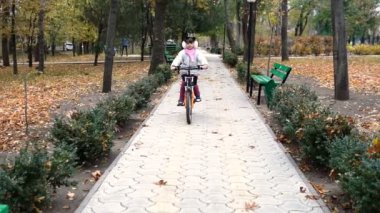 Bir beyaz çocuk sürmek Sonbahar Park yol bisiklet. Küçük kız parkta siyah turuncu döngüsü sürme. Evlat gider spor bisiklet.