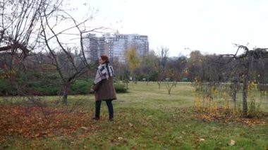 Kadın parkta sarı kaplı ağaçlar arasında yürüyor..