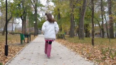 küçük bir kız parkta sonbaharda yürür.