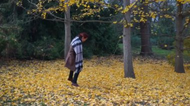 Kadın parkta sarı kaplı ağaçlar arasında yürüyor..