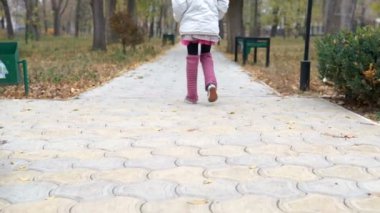 küçük bir kız parkta sonbaharda yürür.