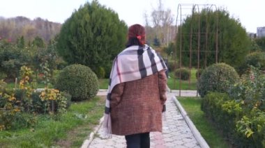 Kadın parkta sarı kaplı ağaçlar arasında yürüyor..