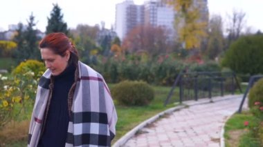 Kadın parkta sarı kaplı ağaçlar arasında yürüyor..