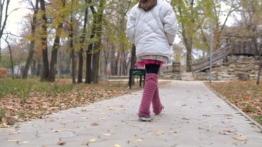 küçük bir kız parkta sonbaharda yürür.