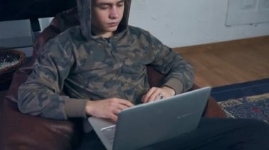 Evde dizüstü bilgisayarla çalışan genç bir adam. Uzaktan çalışma, serbest çalışma