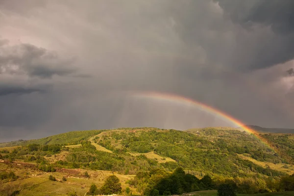 Schönes Gebirgstal mit grünen Hügeln und riesigem Regenbogen — Stockfoto