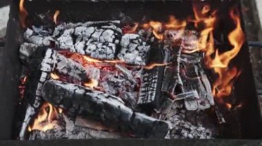 Izgarada kömür yakmak için odun, yakın çekim. Odun kütükleri ızgarada yanıyor, ateş ızgaradaki ağacı sarıyor, alev, ateş.