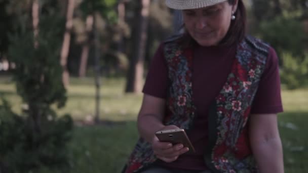 戴着帽子的年轻黑发在城市夏季公园里用手机 — 图库视频影像