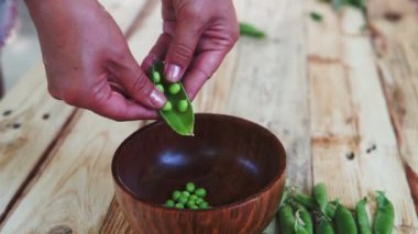 kahverengi çanak, ahşap masa üzerinde kadın el depod yeşil bezelye closeup.