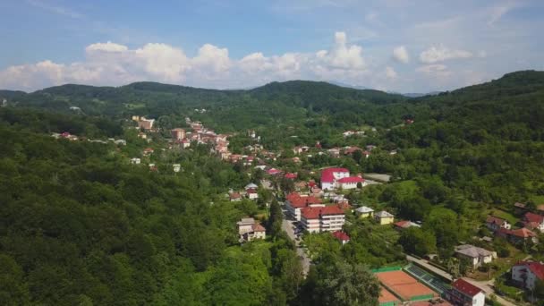 O drone voa sobre a floresta verde e a cidade pequena na área montanhosa dia ensolarado na estação do verão. Carpatians mountains, Roménia . — Vídeo de Stock