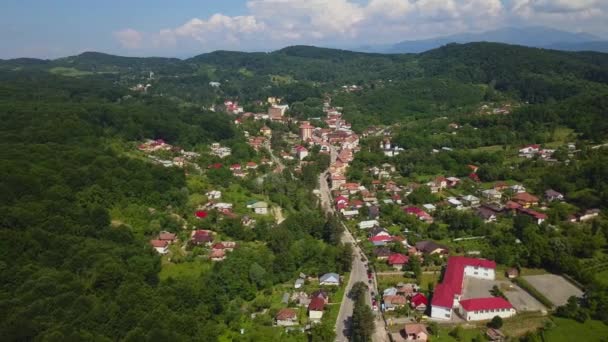 Drone vuela sobre el bosque verde y la pequeña ciudad en la zona montañosa día soleado en temporada de verano. Carpatians mountains, Rumania . — Vídeos de Stock