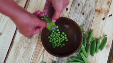 kahverengi çanak, ahşap masa üzerinde kadın el depod yeşil bezelye closeup.