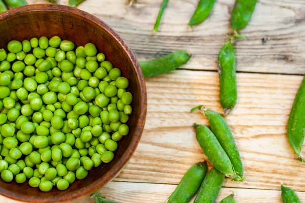 Primer plano guisantes verdes en plato marrón, sobre mesa de madera . —  Fotos de Stock