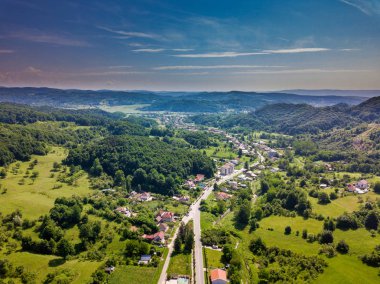 Yaz sezonunda Dağlık alan güneşli gün yeşil orman ve küçük şehir üzerinde drone görünümü. Carpatians Mountains, Romanya.