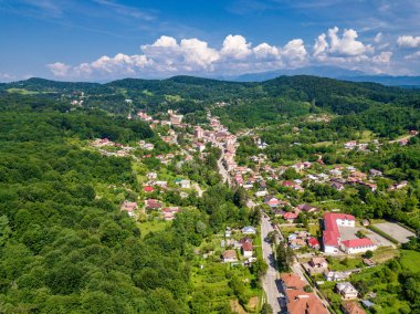 Yaz sezonunda Dağlık alan güneşli gün yeşil orman ve küçük şehir üzerinde drone görünümü. Carpatians Mountains, Romanya.