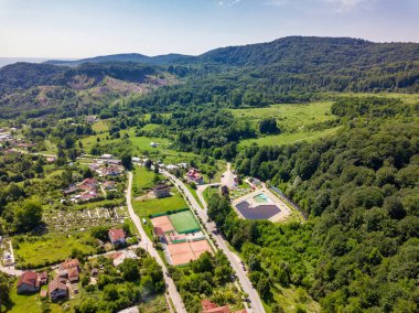 Yaz sezonunda Dağlık alan güneşli gün yeşil orman ve küçük şehir üzerinde drone görünümü. Carpatians Mountains, Romanya.