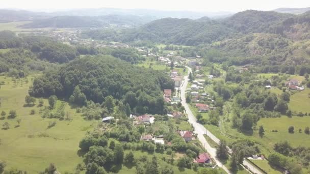 O drone voa sobre a floresta verde e a cidade pequena na área montanhosa dia ensolarado na estação do verão. Carpatians mountains, Roménia . — Vídeo de Stock