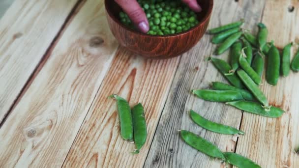 Closeup of woman hand depod green peas in brown dish, on wooden table. — Stock Video