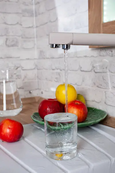 O vidro é preenchido com água da torneira na cozinha — Fotografia de Stock