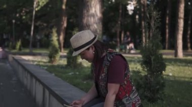 bir şapka genç esmer bir şehir yaz parkında bir cep telefonu kullanıyor