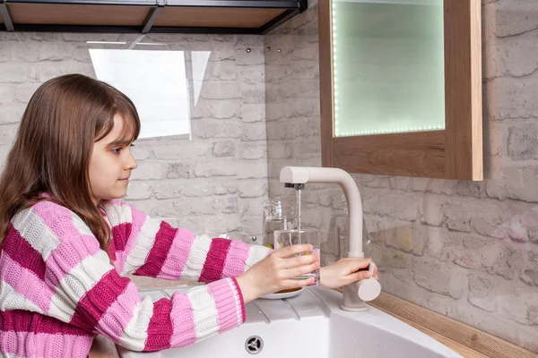 Flickan plockar upp ett glas vatten i köket — Stockfoto