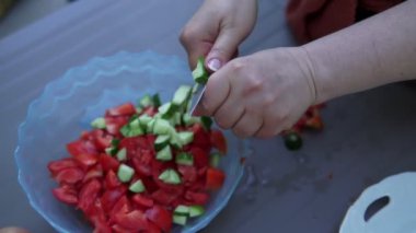 Kadın taze sebzelerden salata hazırlıyor. O mutfakta domates ve salatalık ıslak elleri kesiyor, eller closeup.
