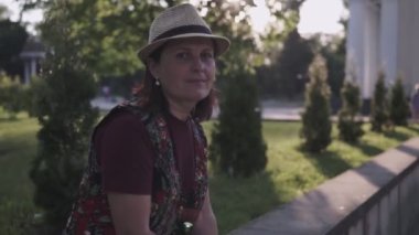 bir şehir yazlık parkta oturan ve kameraya bakarak şapkalı bir bayan ın yakın çekim portresi
