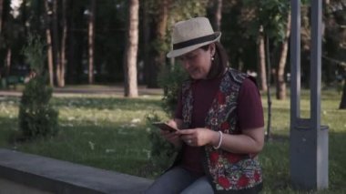 bir şapka genç esmer bir şehir yaz parkında bir cep telefonu kullanıyor