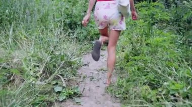bluz ve kot şort arka görünüm kız yeşil orman boyunca yol boyunca yürüyor. Yavaş hareketler.