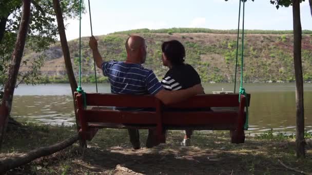 一个男人和一个女人坐在木秋上放松 欣赏河流景观 — 图库视频影像