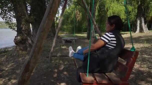 Brunet Haired Woman Enjoys Swinging Wooden Swing Looks Sparkling River — Stock Video