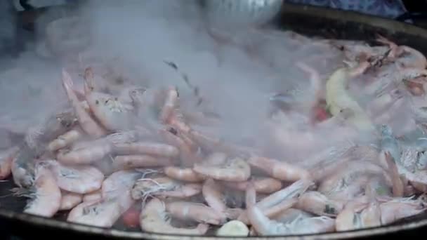 Повар перемешивает и жарит очищенные креветки на большой сковороде — стоковое видео