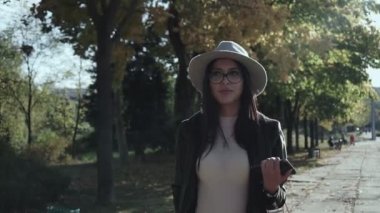 Sonbahar parkında şapkalı ve gözlüklü genç bir esmer yürüyor.