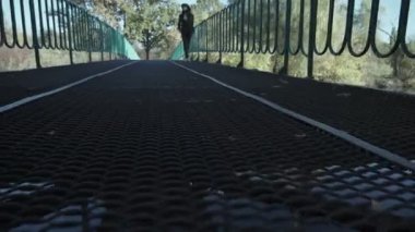Şapkalı çekici genç bir kadın bir sonbahar parkında bir gölün üzerindeki köprü boyunca yürüyor. Sonbaharda parkta yürürken sarı yaprakların üzerinde güzel bir kadının sonbahar portresi.