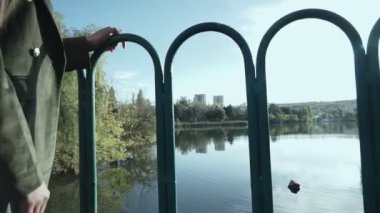 Şapkalı çekici genç bir kadın bir sonbahar parkında bir gölün üzerindeki köprü boyunca yürüyor. Sonbaharda parkta yürürken sarı yaprakların üzerinde güzel bir kadının sonbahar portresi.