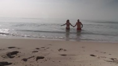 Bir adam ve bir kadın el ele tutuşarak sudan çıkarlar. Deniz kenarında harika bir tatil..
